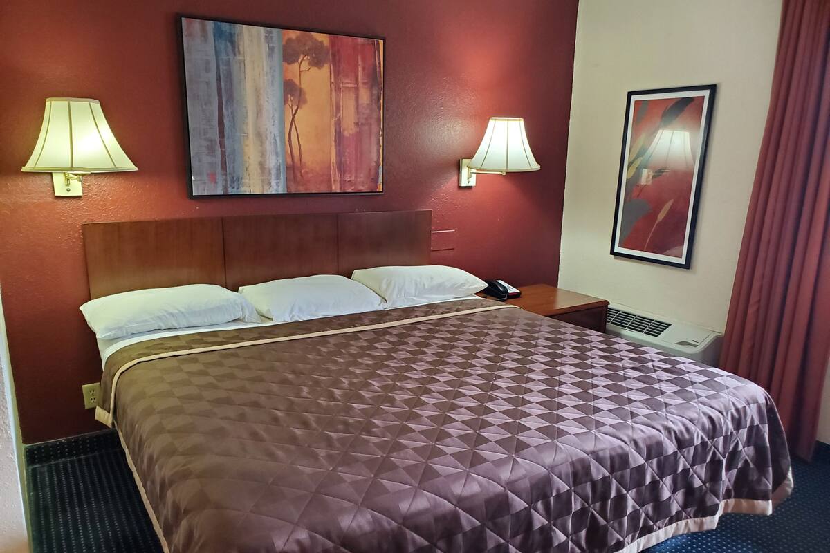 Quarto de hotel com uma cama grande, duas luminárias de cabeceira, um quadro na parede e um telefone na mesinha de apoio.
