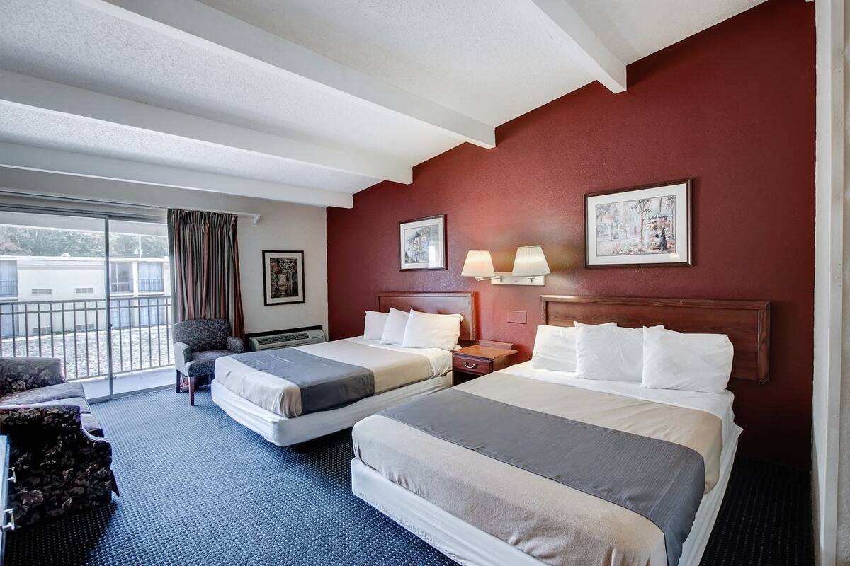 Quarto de hotel com duas camas, um sofá, uma varanda e obras de arte nas paredes.