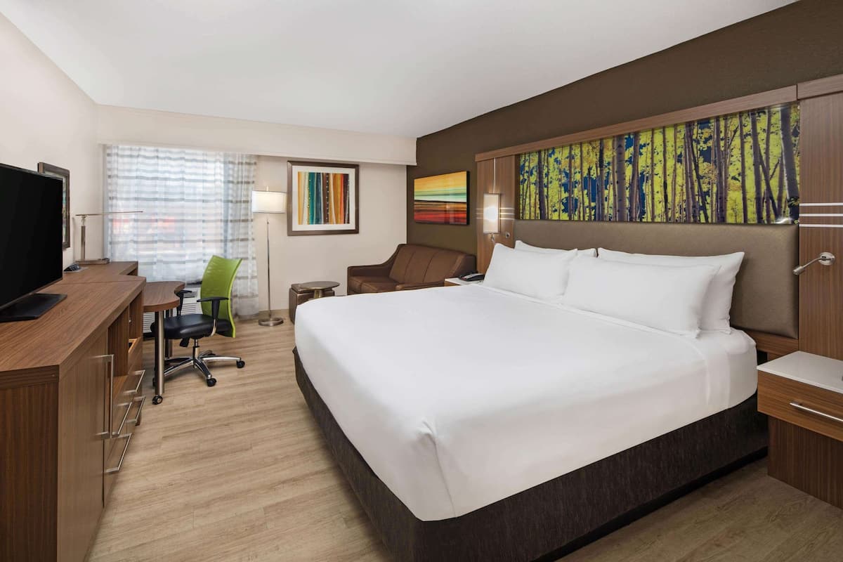 A hotel room with a large bed, a desk with a chair, a television, and artwork on the walls.