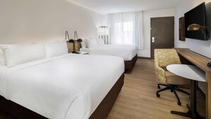 Une chambre d’hôtel avec deux lits, un bureau, une chaise, une télévision et une porte.