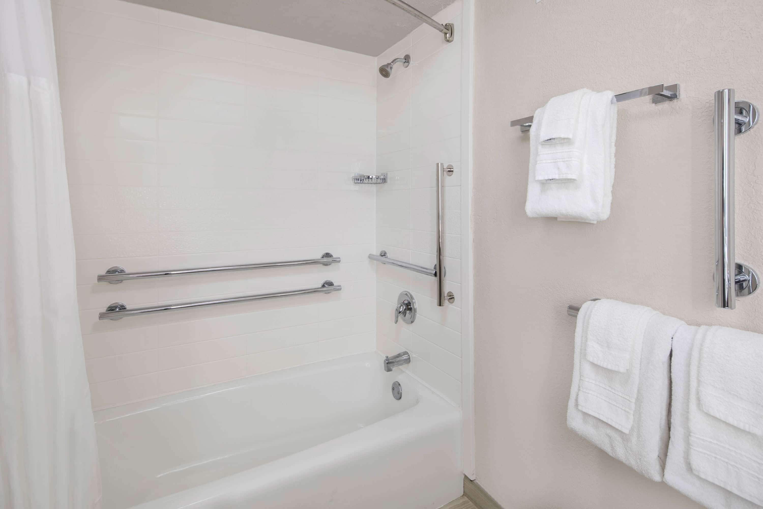 Un baño moderno con cabina de ducha, barras de apoyo, bañera y perchero para toallas.