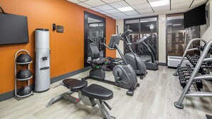 Une salle de sport équipée de matériel d’exercice, d’un banc et d’un téléviseur fixé au mur.