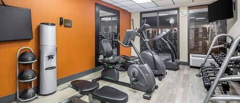 Un gimnasio con equipo de ejercicio, una banca y un televisor instalado en la pared.