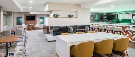 Un área de descanso moderna con una mesa larga y sillas, una chimenea y una zona de bar con taburetes.