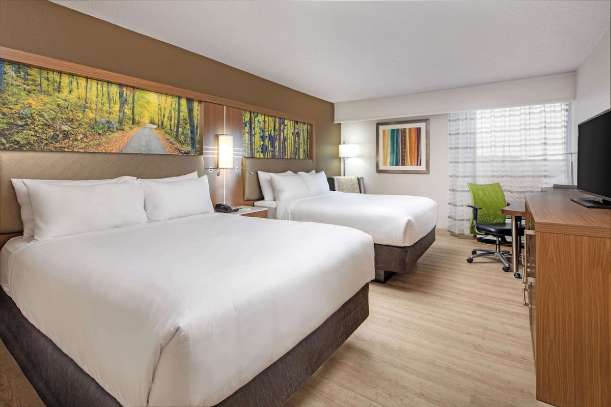 A hotel room with two beds, a desk, a chair, a TV, and artwork on the walls.