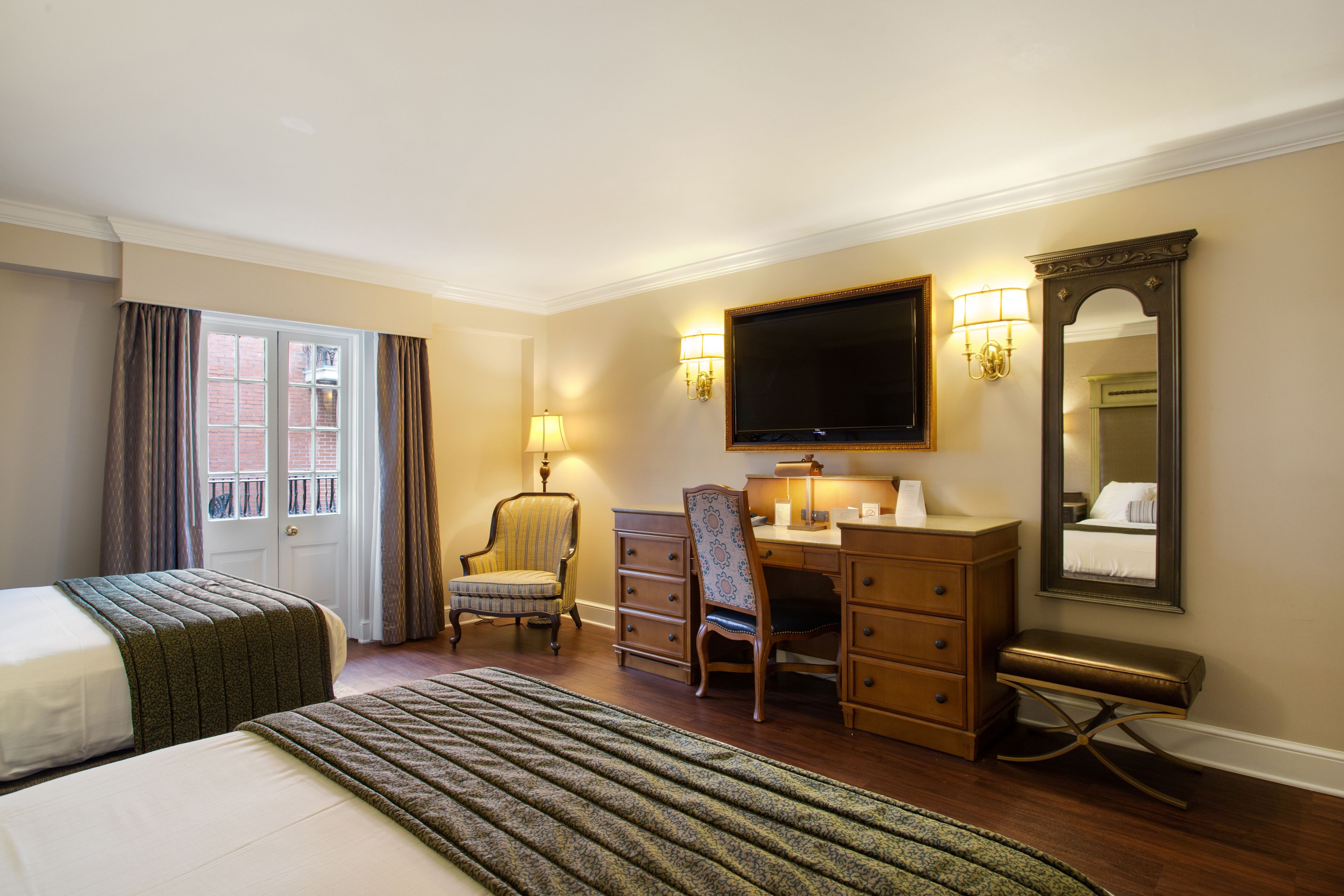 Ein Hotelzimmer mit zwei Betten, einem Schreibtisch, einem Stuhl, einem Schminktisch und einem Spiegel.