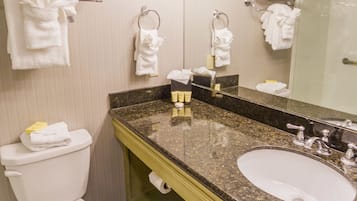 A bathroom with a toilet, sink, and mirror. There are towels hanging on the wall and a shelf with towels.