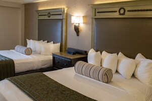 A hotel room with two beds, a nightstand with a clock, a wall-mounted lamp, and a decorative wreath.