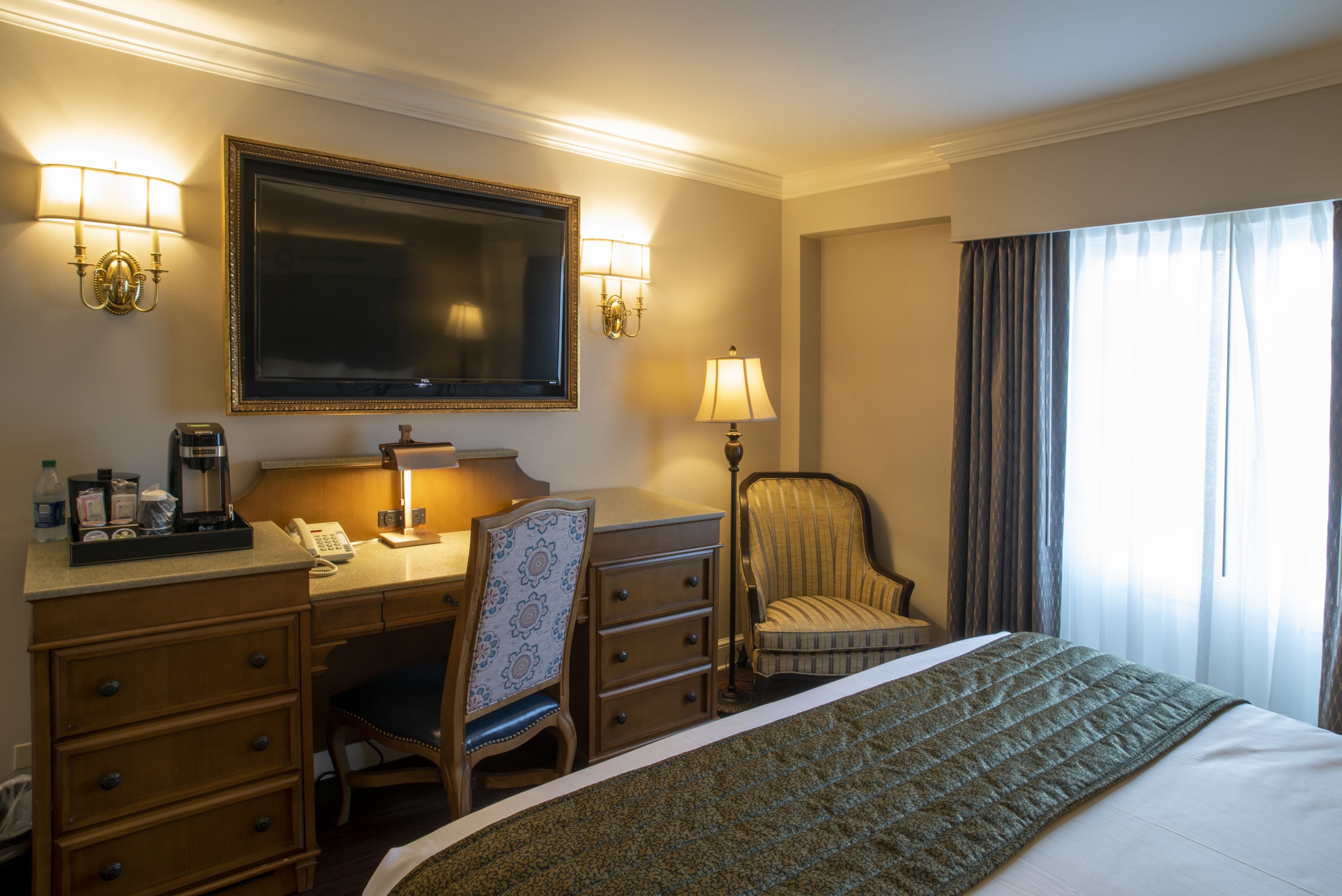 Een hotelkamer met een bed, een bureau met telefoon, een stoel, een lamp en een grote spiegel.