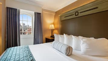 Quarto de hotel com uma cama grande, janela com cortinas, mesa de cabeceira com abajur e vista da cidade.