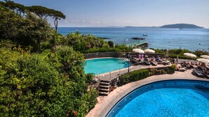 A pool area with a view of the sea, surrounded by lush greenery.