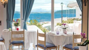 A seaside restaurant with white tables and chairs, blue curtains, and potted plants.