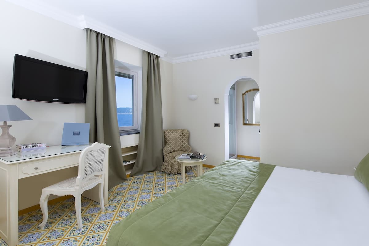 Une chambre d’hôtel avec un lit, un bureau avec un ordinateur portable, une chaise, une télévision et une fenêtre avec des rideaux.