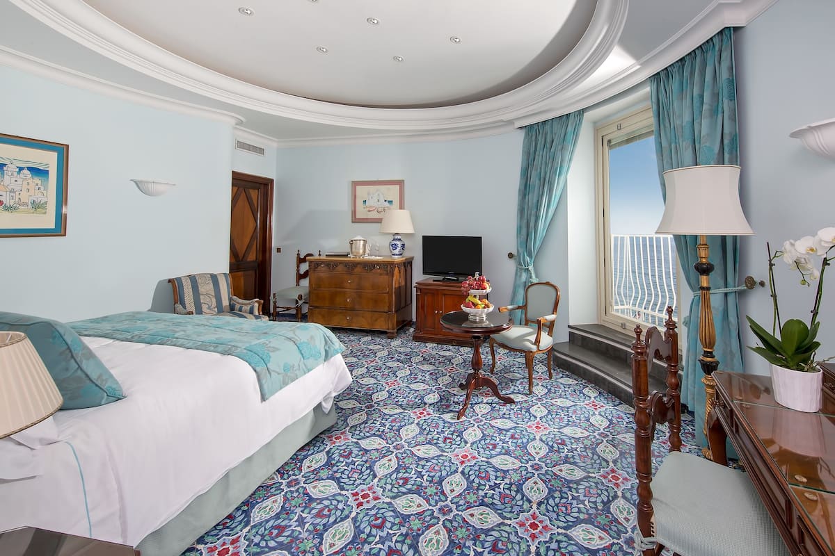 Une chambre d’hôtel avec un grand lit, une commode en bois, une télévision et une fenêtre avec des rideaux.