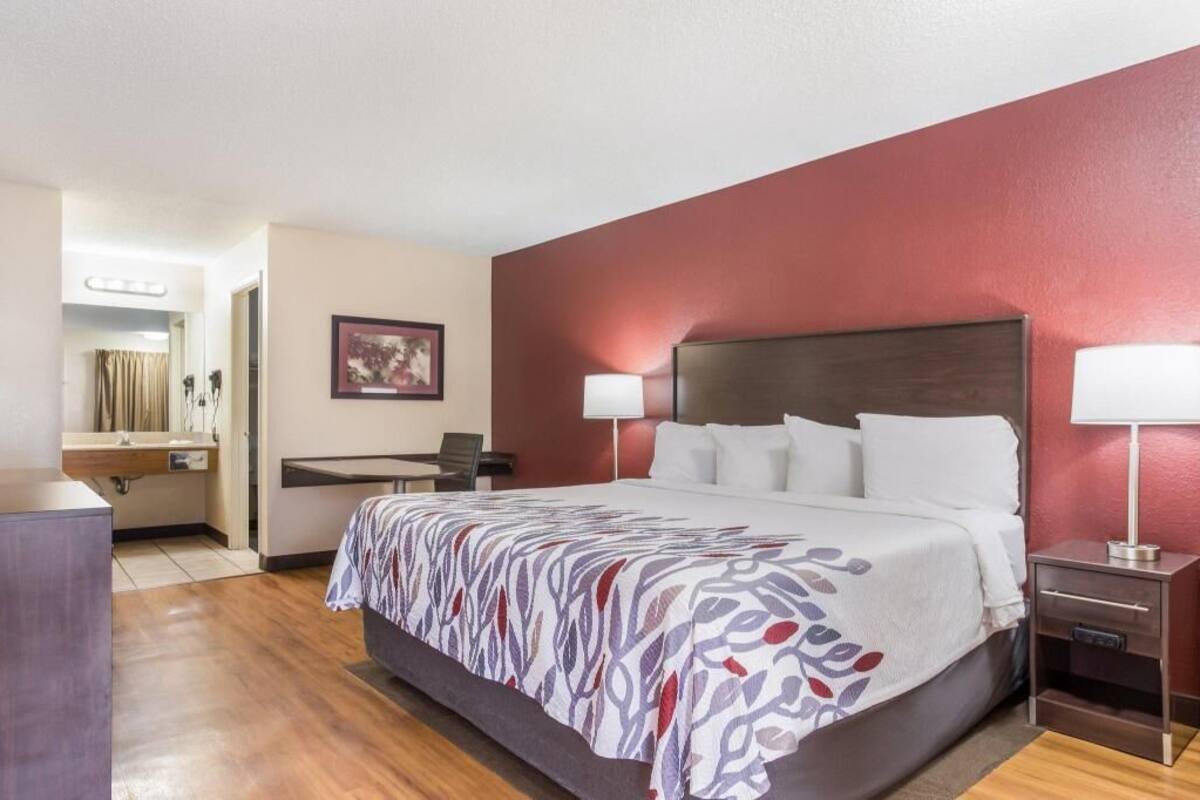 A hotel room with a bed, bedside lamps, a desk with a chair, a mirror, and a framed picture on the wall.