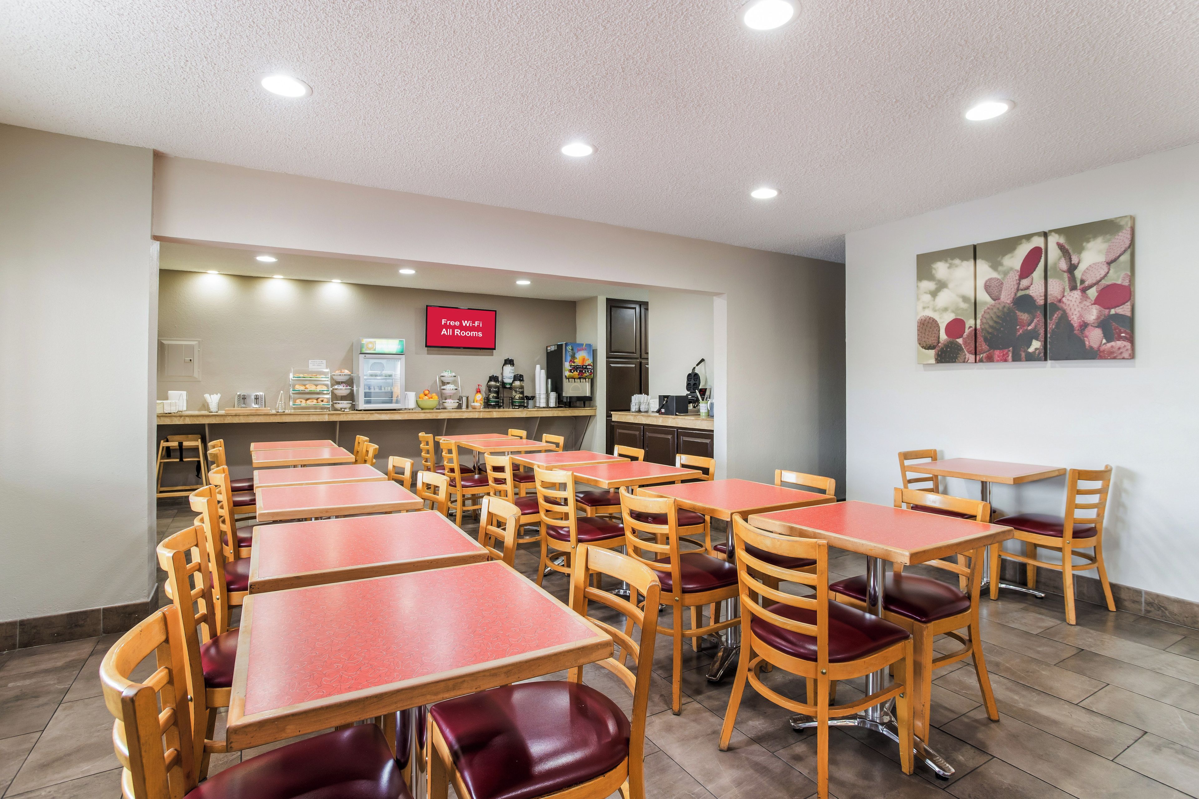 A dining area with multiple tables and chairs, a kitchen area in the background, and a sign indicating free Wi-Fi availability.