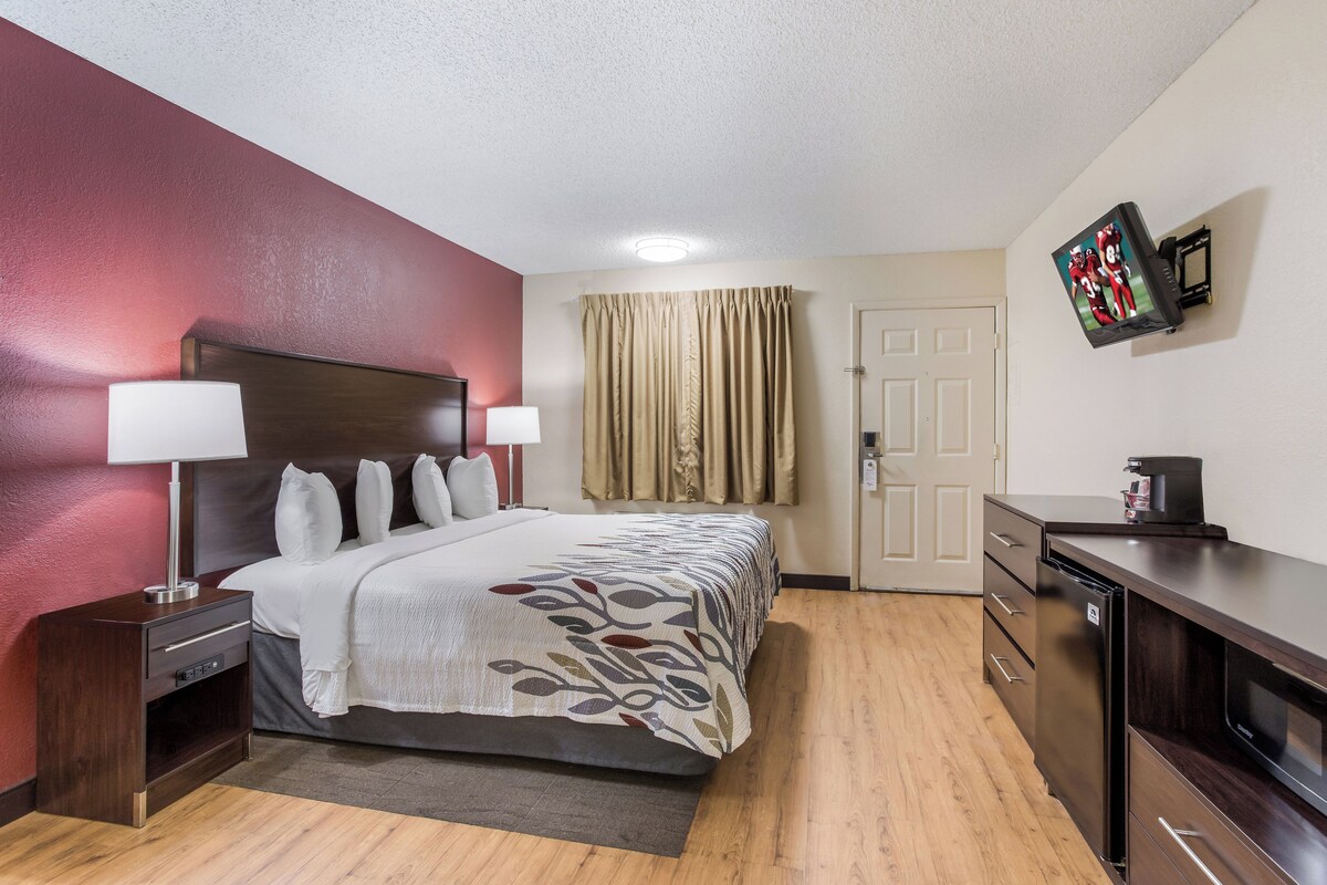 A hotel room with a bed, bedside tables, a desk, a television, and a door.