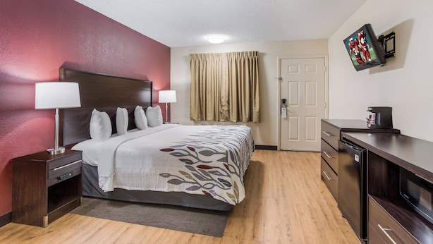 A hotel room with a bed, bedside tables, a desk, a television, and a door.