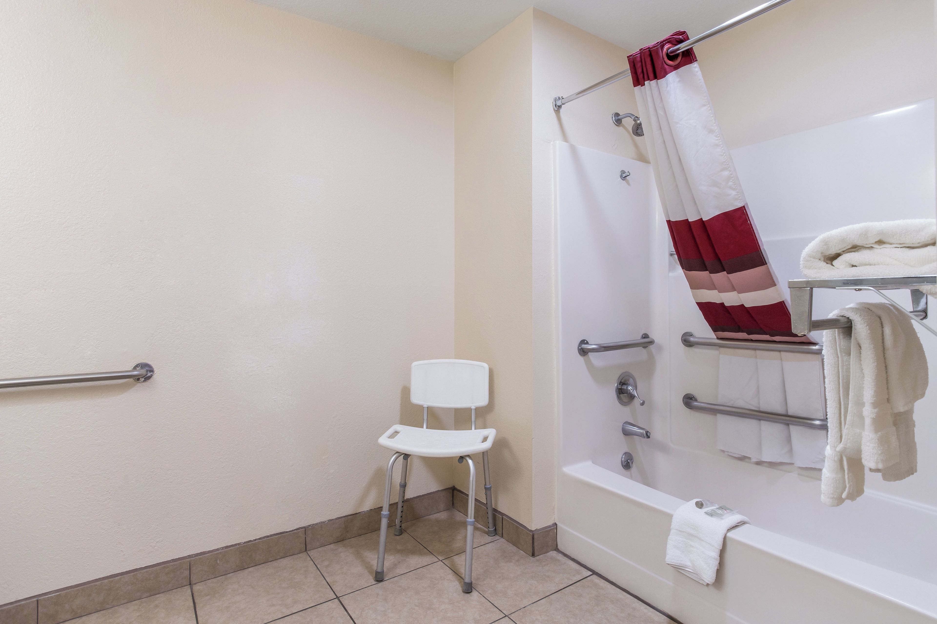 Un baño con una bañera blanca, una ducha con cortina verde y blanca a rayas, una silla blanca y un pasamanos.