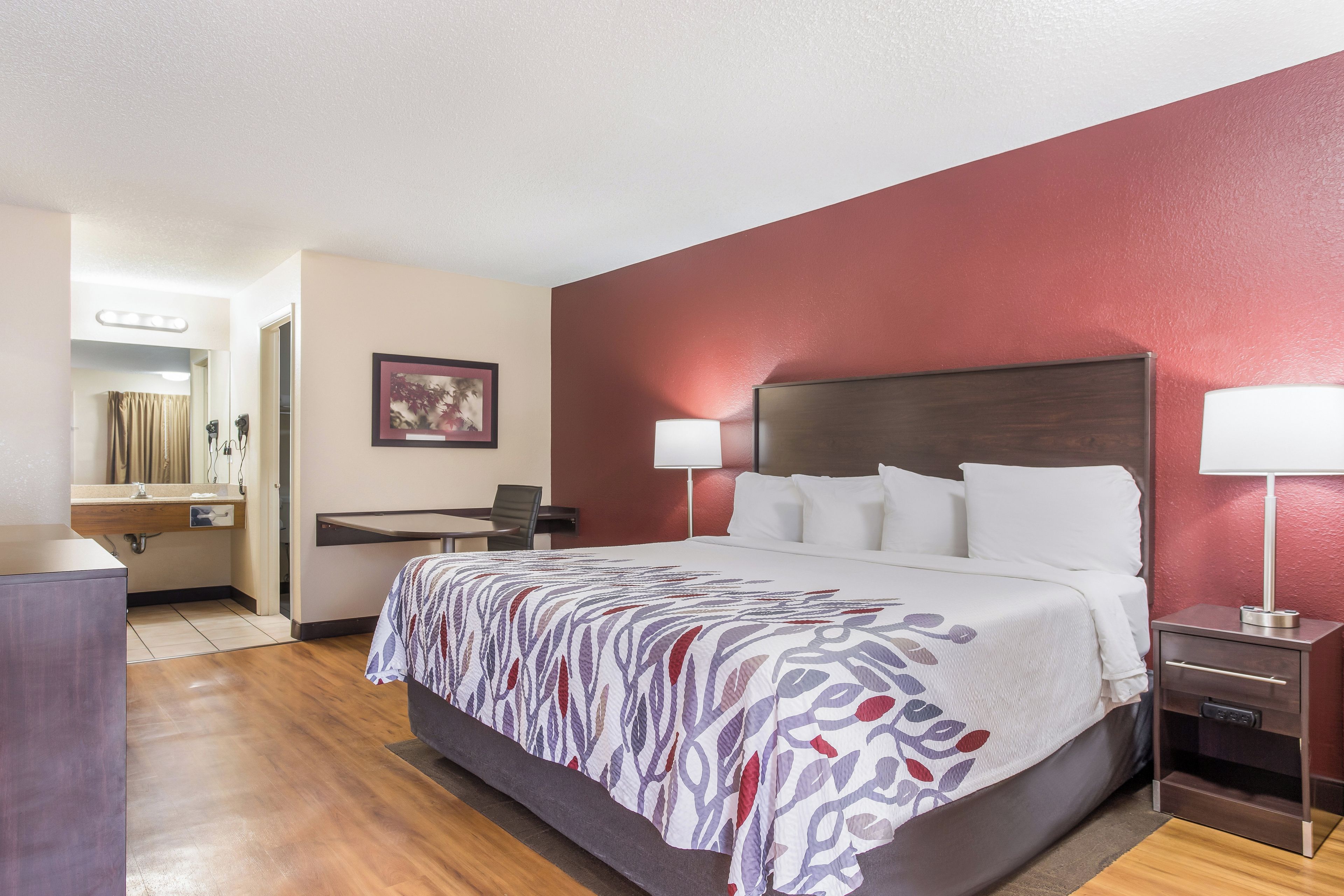 A hotel room with a bed, bedside lamps, a desk, and a mirror.