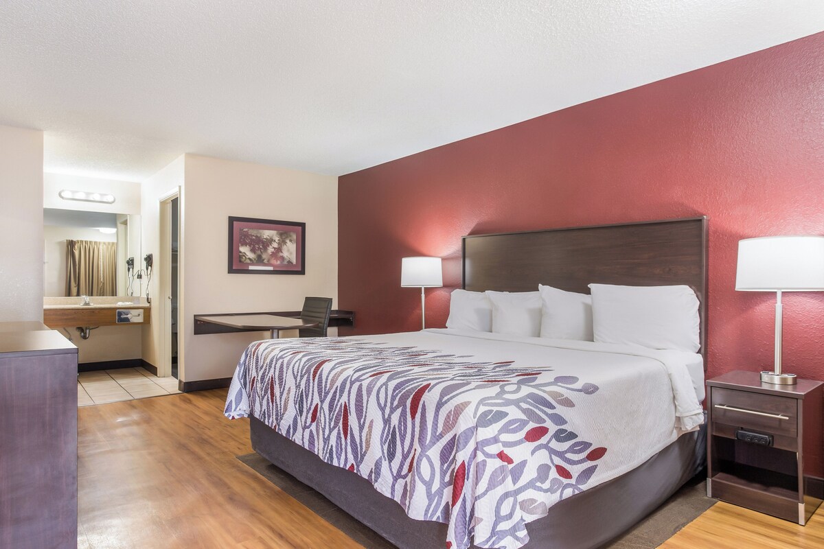 A hotel room with a bed, bedside lamps, a desk, and a mirror.