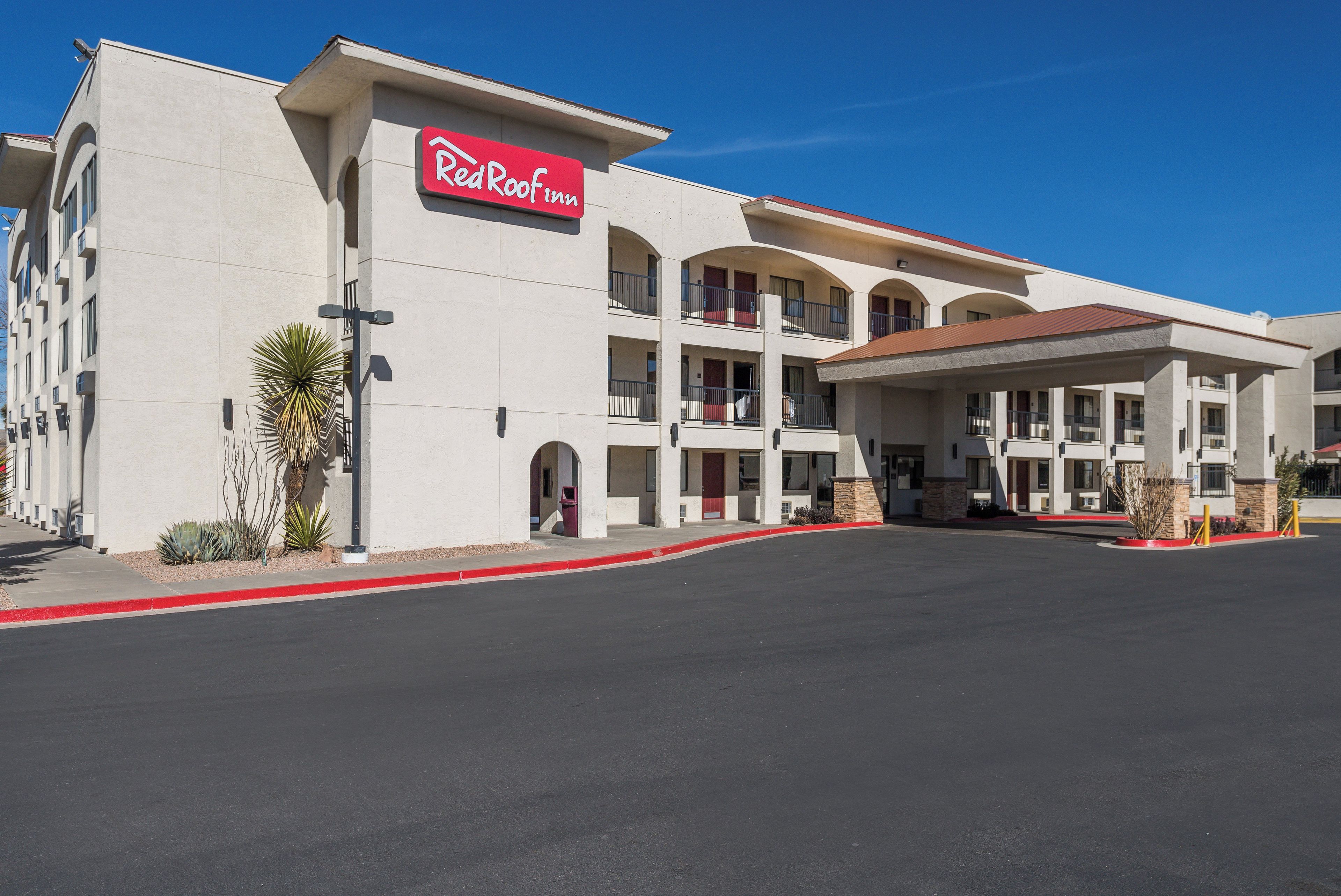 A Red Roof Inn with a multi-story structure, a covered parking area, and a clear sky.
