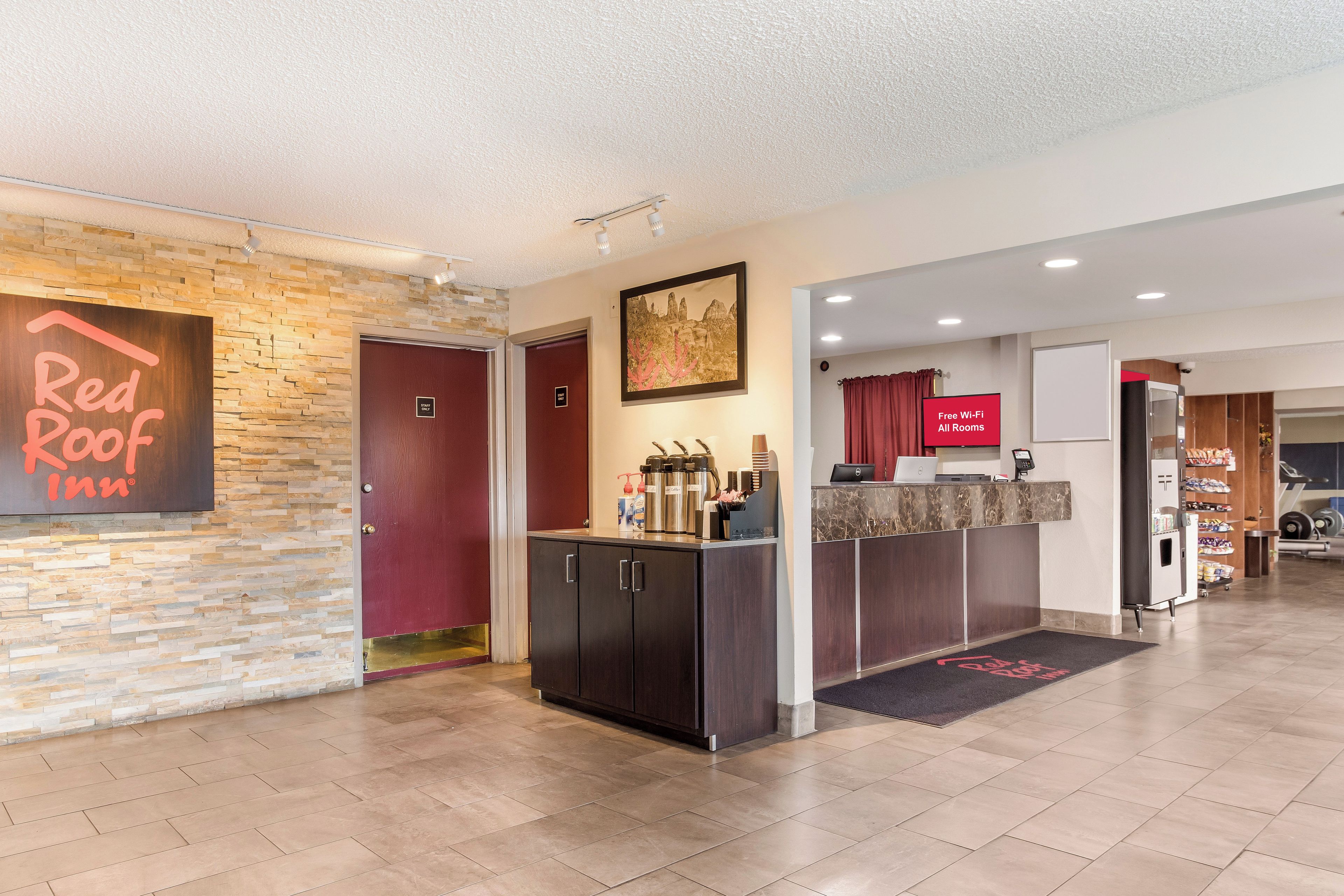 Ein Empfangsbereich eines Red Roof Inn mit Steinwand, Rezeptionstresen und Schild für kostenloses WLAN.