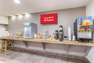 Zona de desayuno autoservicio con refrigerador, máquinas de café y un cartel que indica Wi-Fi gratuito.