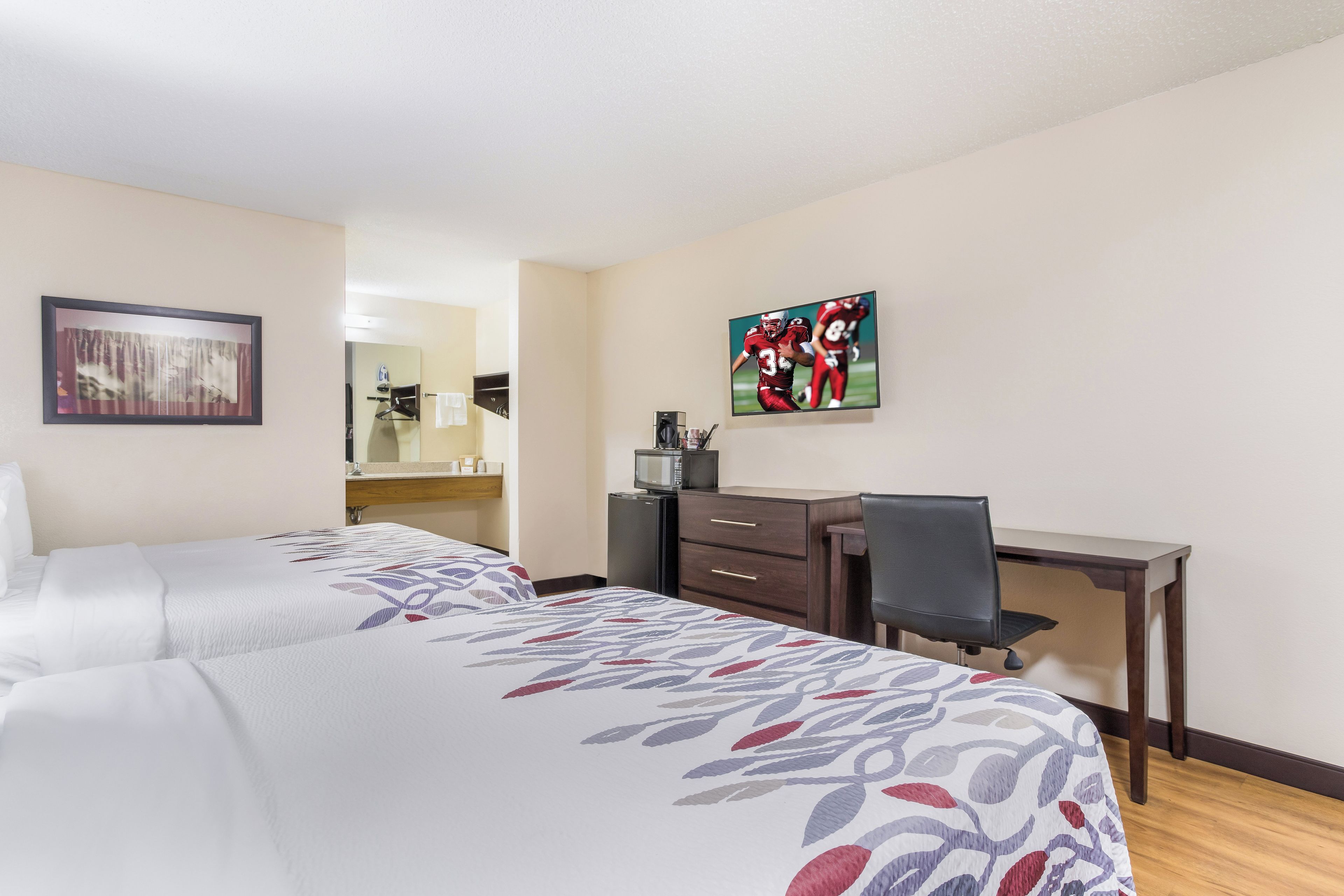 Een hotelkamer met twee bedden, een bureau, een stoel, een magnetron en kunstwerken aan de wanden.