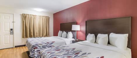 Habitación de hotel con dos camas, una mesita de noche con lámpara, una puerta y una ventana con cortinas.