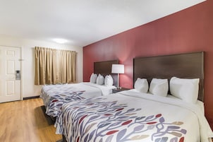 Habitación de hotel con dos camas, una mesita de noche con lámpara, una puerta y una ventana con cortinas.