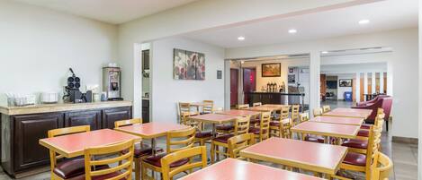 A restaurant with multiple tables and chairs, a counter with a coffee machine, and a painting on the wall.