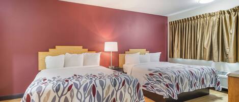 A hotel room with two beds, a nightstand, a lamp, and a window with curtains.