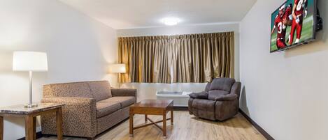 A living room with a sofa, armchair, coffee table, lamp, and a painting on the wall.