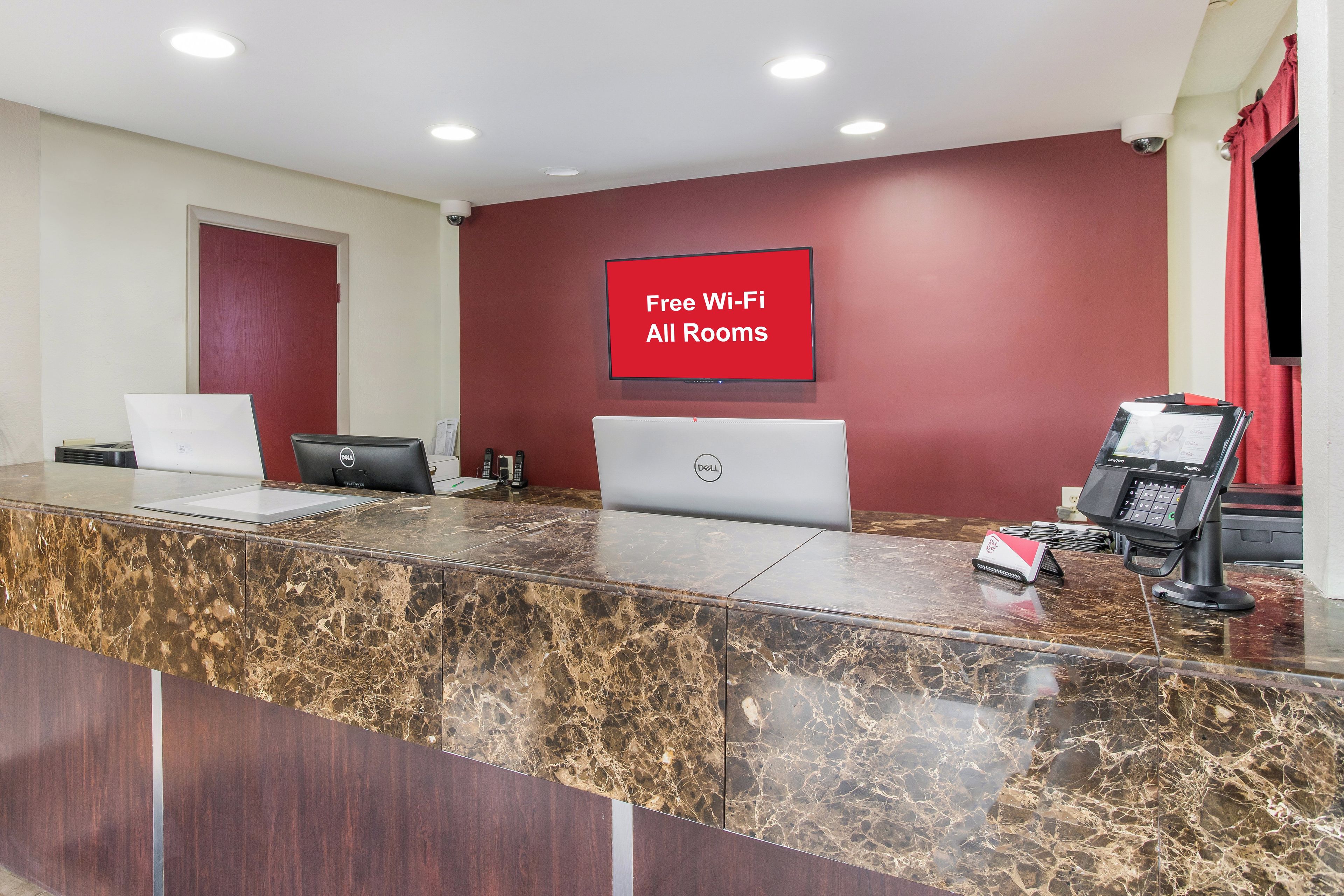 Un comptoir d’accueil d’hôtel avec un revêtement en marbre, un ordinateur portable Dell, un ordinateur de bureau, un téléphone et un panneau indiquant que le Wi-Fi est disponible gratuitement dans toutes les chambres.