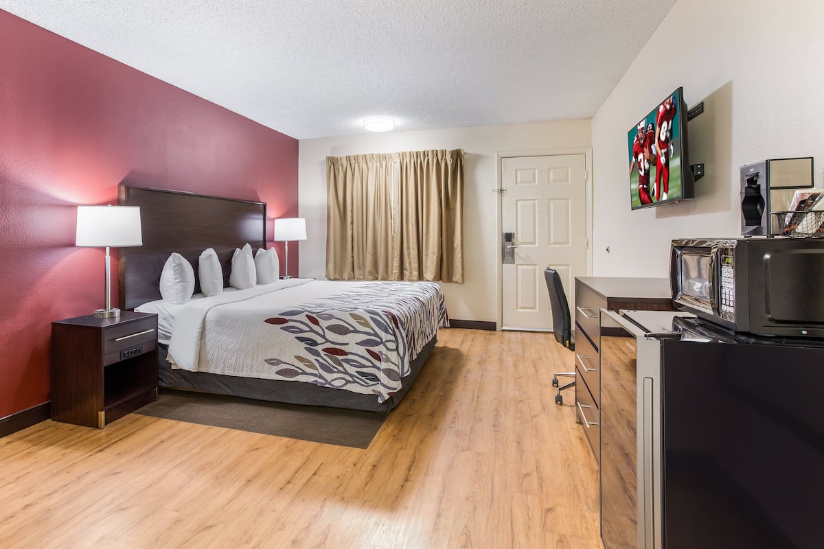 A hotel room with a bed, bedside lamps, a TV, a refrigerator, and a desk with a chair.