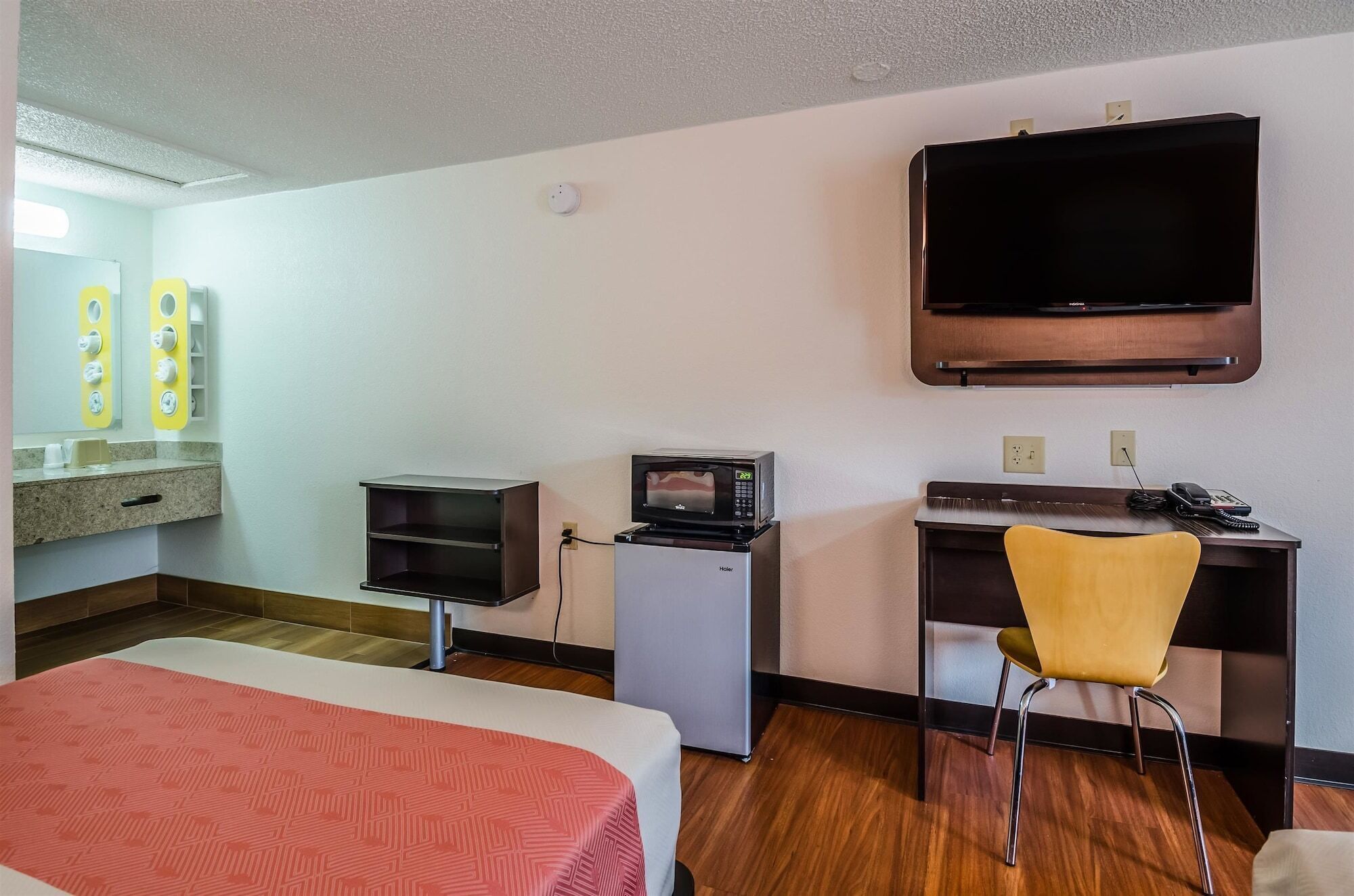 A hotel room with a bed, a desk with a chair, a microwave, a television, and a small kitchenette.