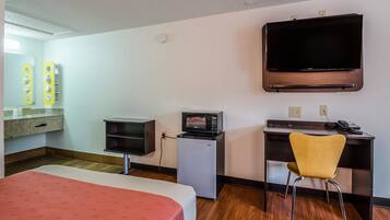 A hotel room with a bed, a desk with a chair, a microwave, a television, and a small kitchenette.