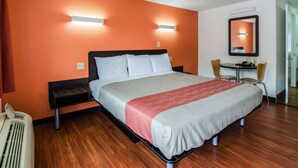 A hotel room with a bed, bedside table, chair, desk, and a mirror.