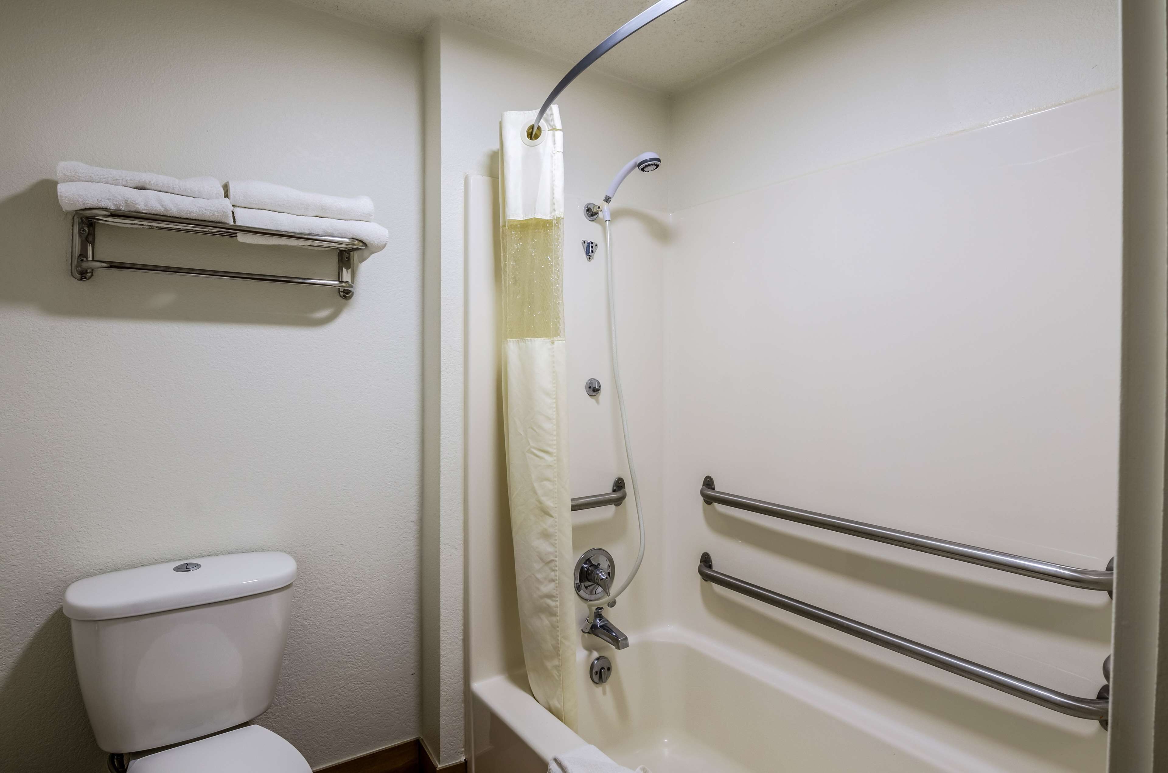 Un baño con inodoro, ducha con barra de apoyo y toallero.