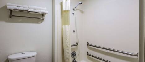 Un baño con inodoro, ducha con barra de apoyo y toallero.