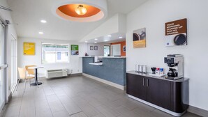 A modern hotel lobby with a reception desk, a coffee machine, and a seating area with chairs. - Motel 6 Troutville, VA (Troutville)