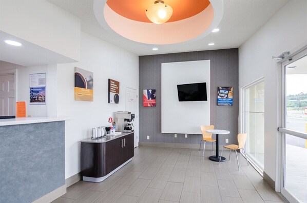 A modern reception area with a coffee machine, a flat-screen TV, and a seating area with two chairs. - Motel 6 Troutville, VA (Troutville)