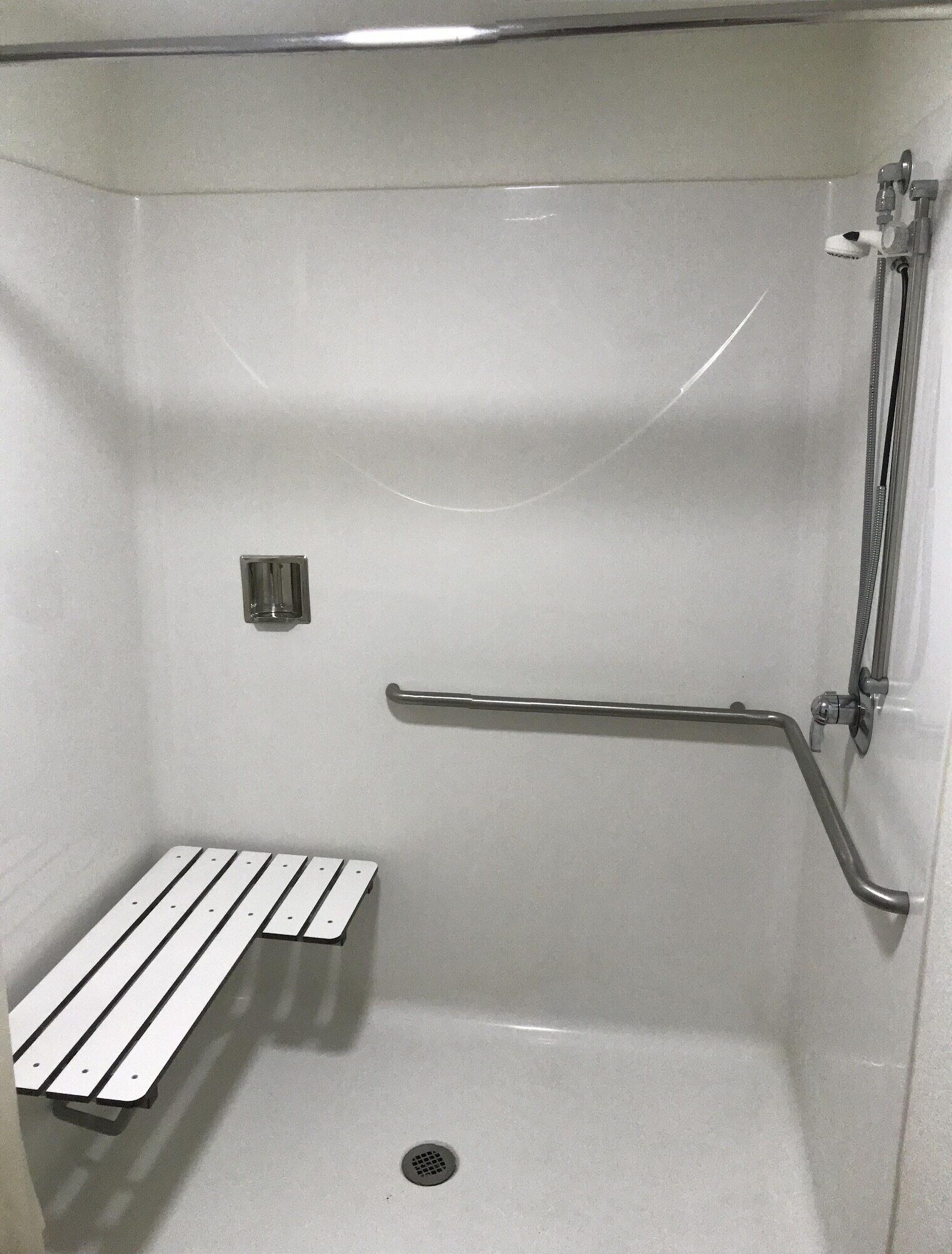 Een douchecabine met een handgreep, een bankje en een handdouche.