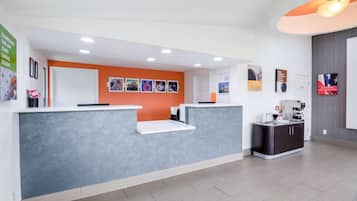 A reception area with a grey reception desk, an orange accent wall, and a coffee machine.