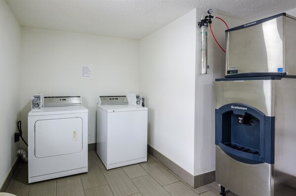 A laundry area with two front-loading washing machines and a stainless steel commercial dryer. - Motel 6 Troutville, VA (Troutville)