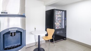 A vending machine with snacks, a Scotman ice dispenser, and a small round table with a chair.