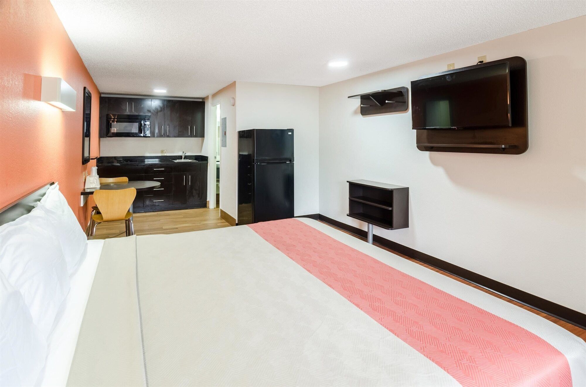 A hotel room with a bed, a small kitchenette, a TV, and a dining area.