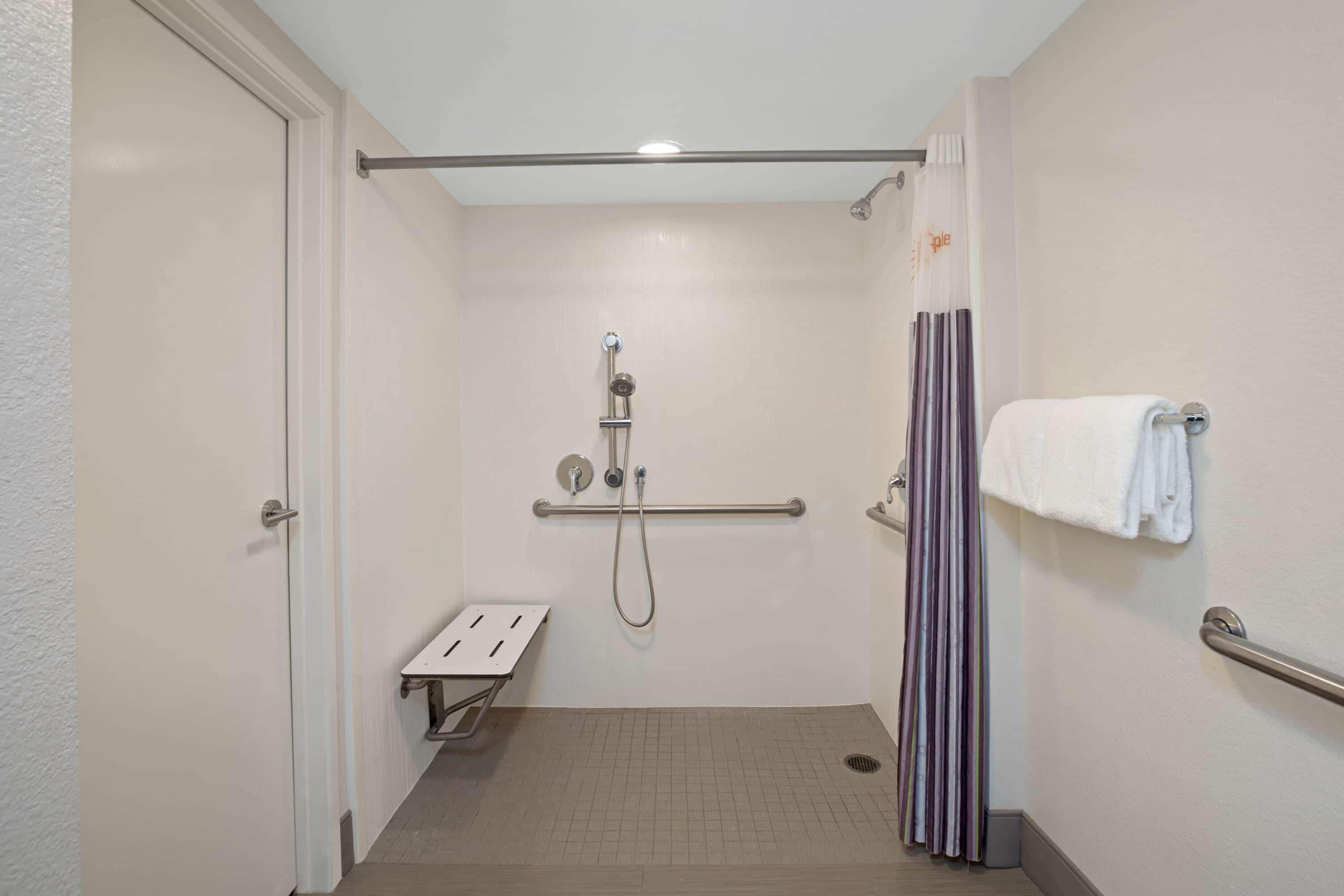 A small, enclosed shower area with a grab bar, a white towel rack, and a bench.