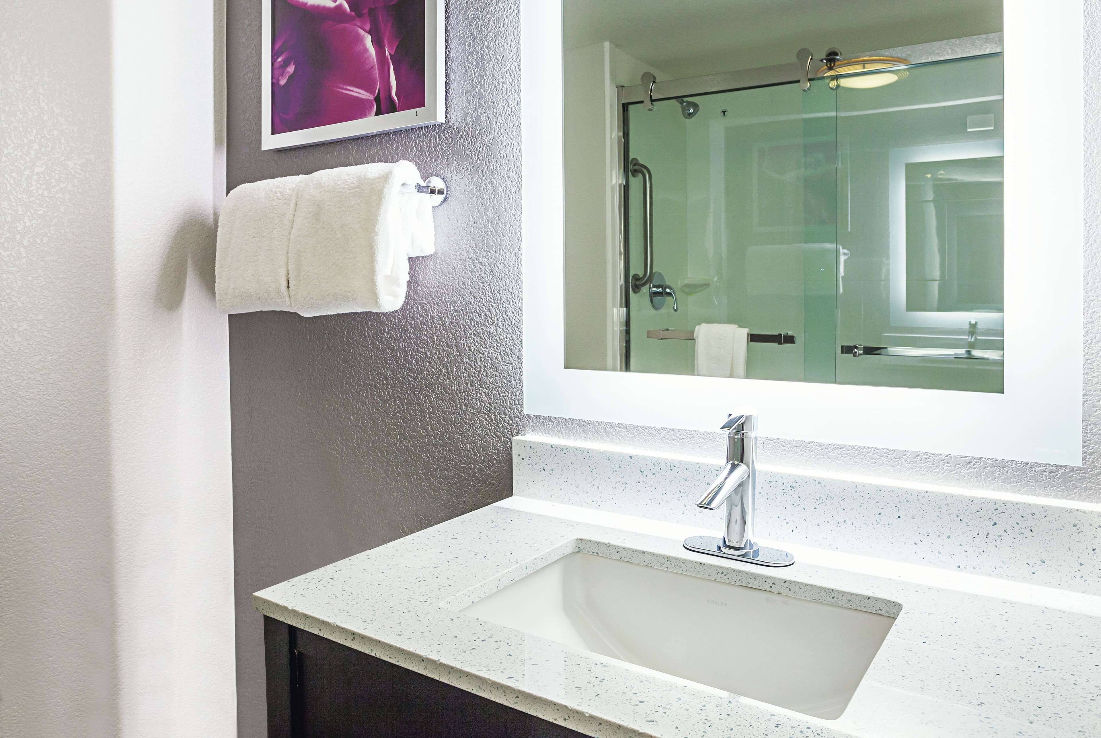 Un baño con un lavabo blanco, cabina de ducha con mampara de vidrio y un cuadro en la pared.